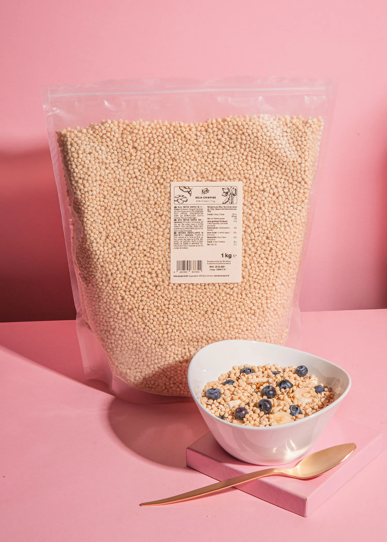 eine weiße Schüssel mit Müsli und Blaubeeren steht neben einem großen Plastikbeutel Müsli